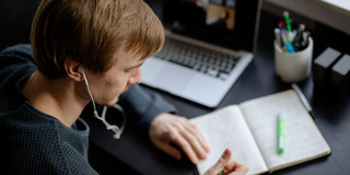 Lernen mit verschiedenen Medien Ein Student arbeitet mit Laptop und Notizbuch.